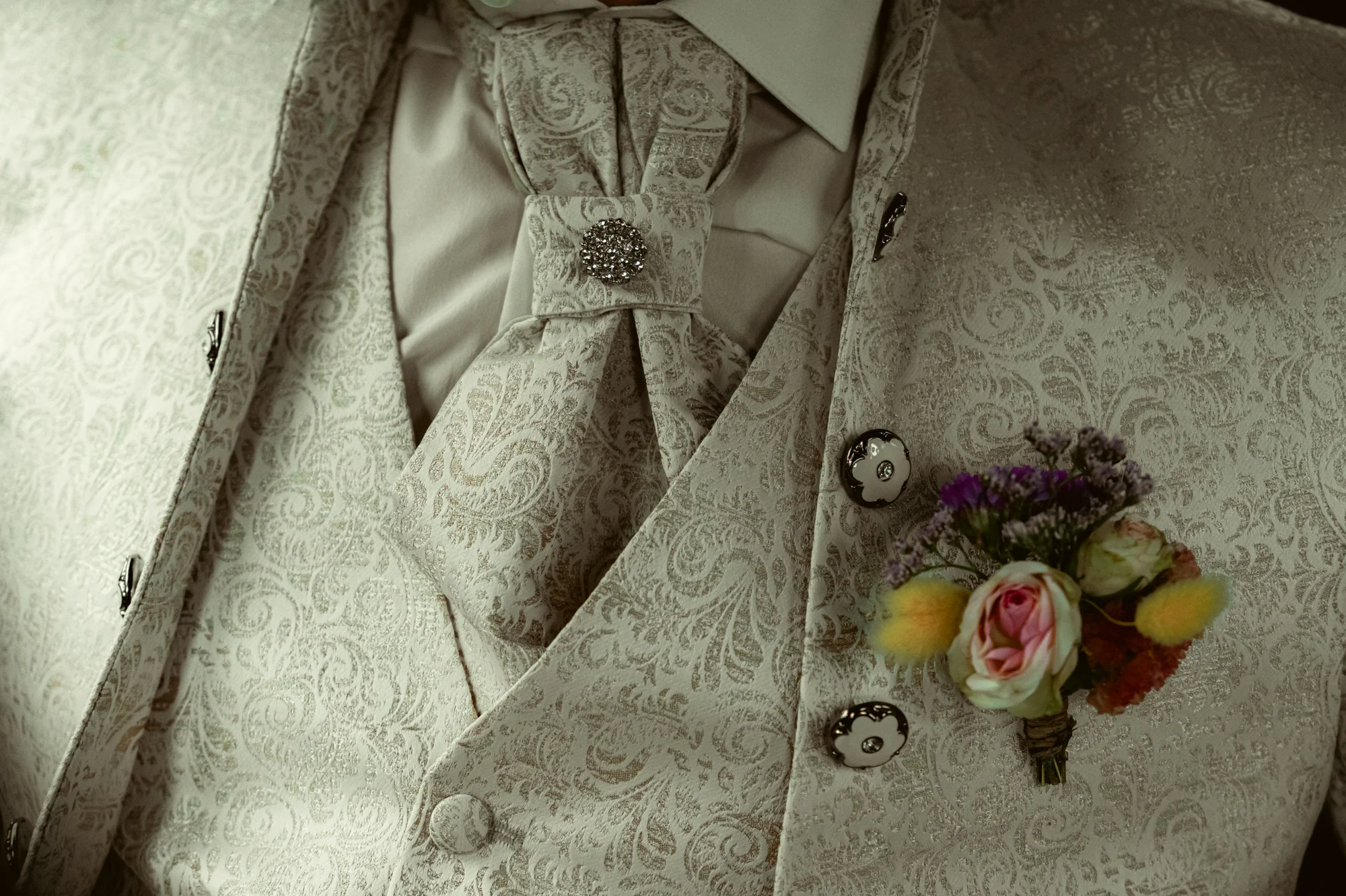 Détail costume jacquard du marié, boutonnière fleurie, cravate lavallière