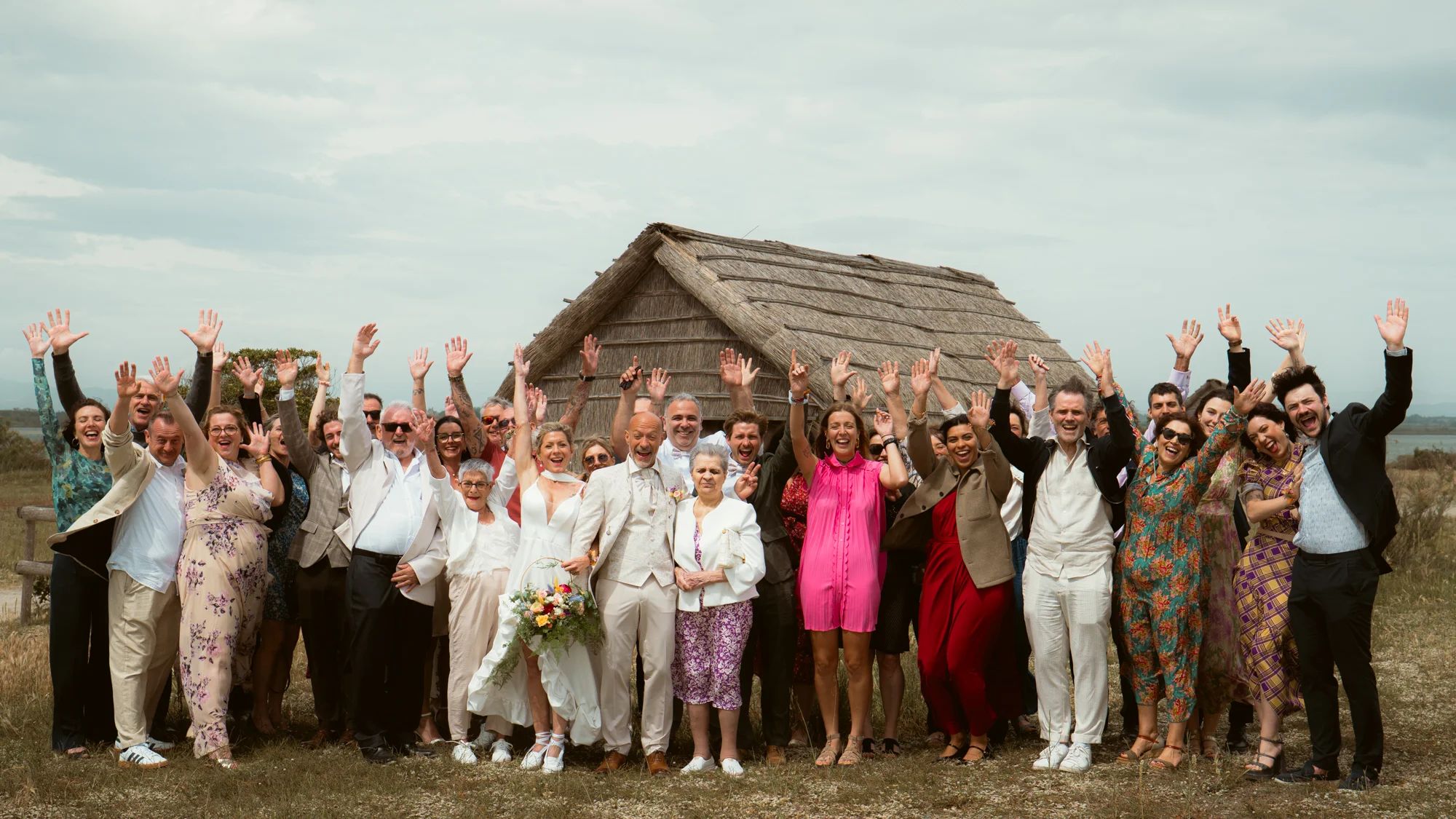 Photo de groupe des invités, mariés au centre, cabane en roseaux, bord d'étang